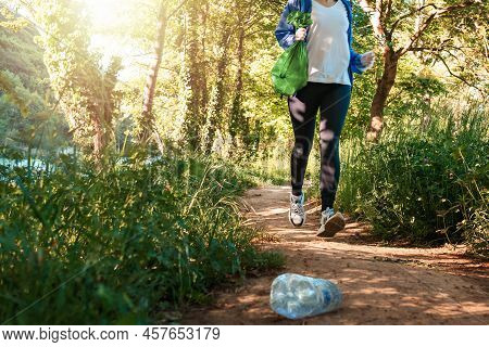 Person In Sportswear Jogging At The Park And Holding A Bag Of Garbage. Low Angle View. The Concept O
