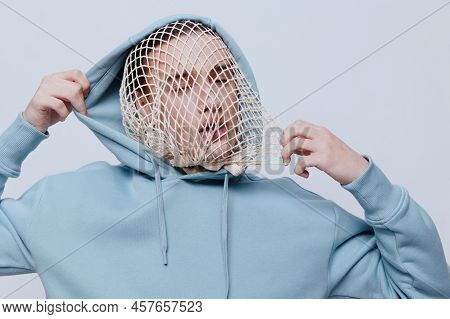 Tortured, Suffering From Problems, A Man With A Mesh On His Face Stands In A Light Blue Hoodie On A 