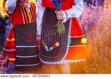 Beautiful Girls In Traditional Bulgarian Folklore Costumes In Lavender Field During Harvest And Suns