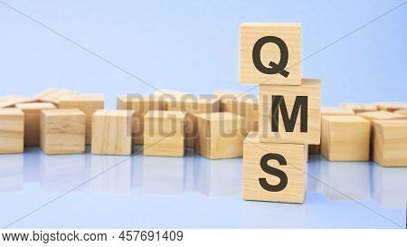 Qms. Wooden Cubes. Blocks Lie On A Black Background. Stacks With Coins. Inscription On The Cubes Is 