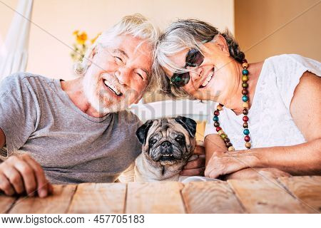 Happy Couple Of Senior Caucasian People Have Fun And Smile With Funny Nice Old Dog Pug In The Middle