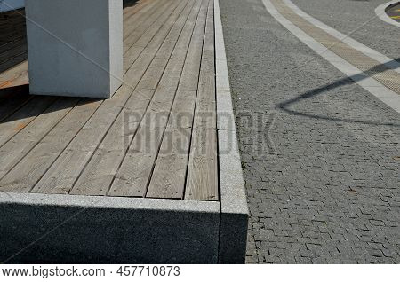 The Wooden Terrace With Planks Is Bordered By A Granite Curb. At The Edge Of The Sidewalk, A Raised 