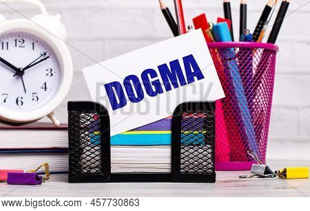 The Office Desk Has Diaries, An Alarm Clock, Stationery, And A White Card With The Text Dogma. Busin
