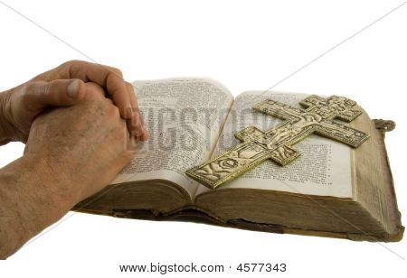 Ruce v modlitbě a kříž na otevřené Bibli