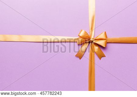 Top View Of Gold Ribbon Rolled And Yellowbow Isolated On Colored Background. Flat Lay With Copy Spac