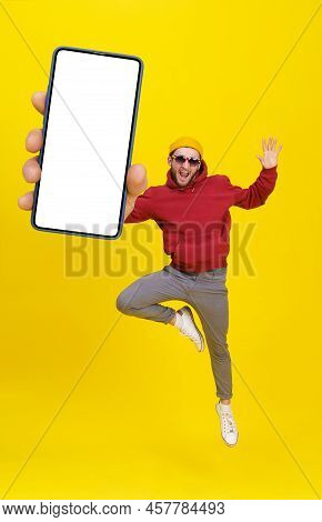 Young Man In Uk Flag Sunglasses Jumping In Joy Like Ballet Dancer Holding Smartphone Wearing Casual 