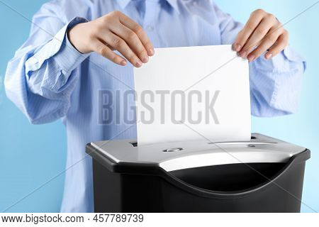 Woman Destroying Sheet Of Paper With Shredder On Light Blue Background, Closeup