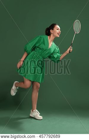 Portrait Of Beautiful Young Girl Posing In Dress, Playing Badminton Isolated Over Green Studio Backg