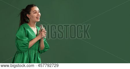 Portrait Of Beautiful Young Girl Posing In Dress, Singing In Microphone Isolated Over Green Studio B