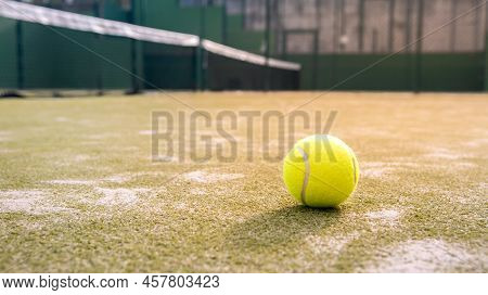 Yellow Ball On Floor Behind Paddle Net In Green Court Outdoors. Padel Tennis