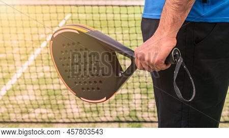 One Caucasian Man With Black Padel Racket Behind The Net Court. Sport Concept