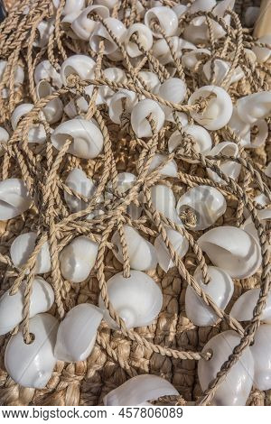 White Shells Strung Like Beads On A Rope Lie On A Mat On The Beach. Beach Decor On A Warm Sunny Day 