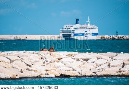 Bari, Puglia, Italy - August 29 2021: Tanned Bather Sunbathing On The Breakwater With Pier, Cruise S