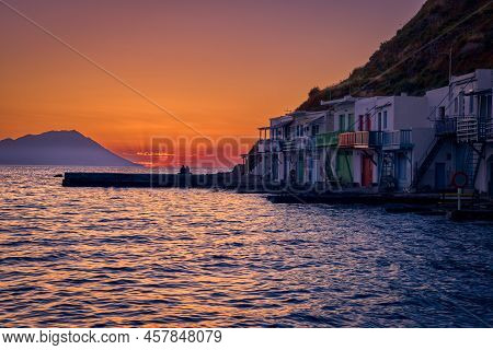 Sunset In Fishermen Village Of Klima, Milos Island, Greece. Pair Of Adults Enjoy Sunset View On Pier