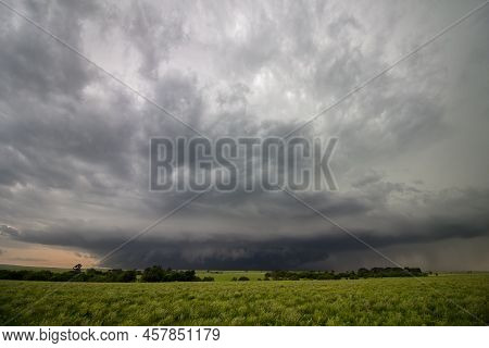 A Strong Thunderstorm Looms On The Horizon Over A Green Field In Kansas.