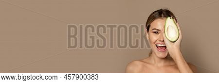 Beautiful Woman Covers Half Of Her Face With Half An Avocado. Beauty And Skin Care Concept. Web Bann