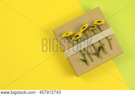 Five Tiny Yellow Flowers Tied To The Square Kraft Gift Box With Linen Ribbon. Flat Lay, Top View On 
