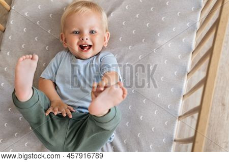 Upper View Of Sweet Carefree Baby Having Fun Touching His Toes In Bed Putting Legs Up