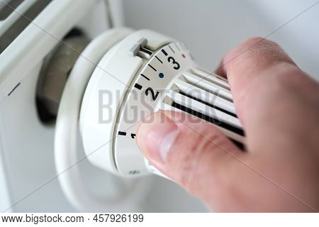 Person Adjusting Thermostat On Radiator To Lower Temperature, Saving Energy And Money Concept