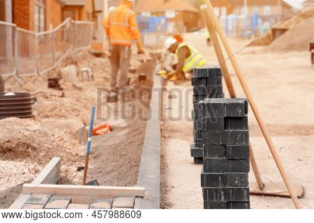 Builders Installing Paving Blocks During Road And Footpath Construction On A Semi-dray Concrete Mix.
