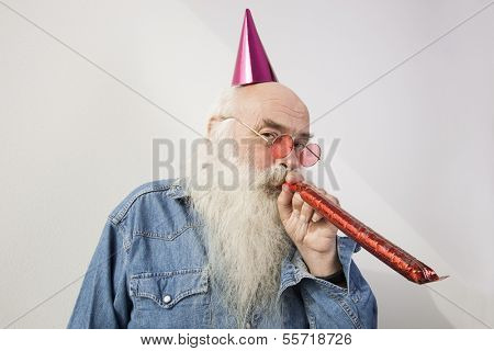 Portrait of senior man wearing party hat while blowing horn against gray background