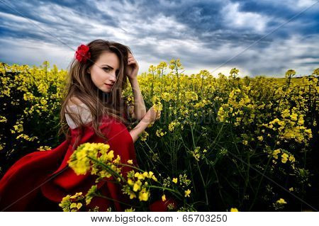 beautiful woman with red cloak on blooming rapeseed field in summer
