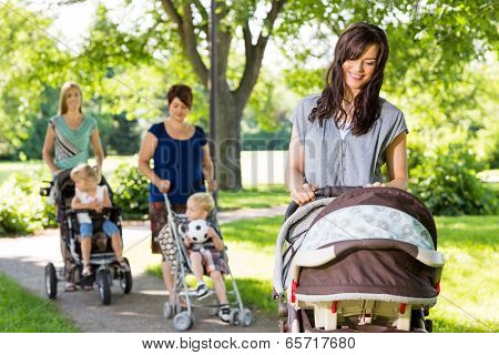 Young mother looking at baby in stroller at park with friends and children in background
