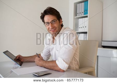 Casual smiling businessman using tablet and calculator in his office