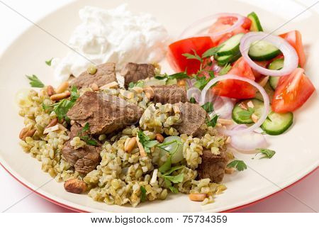 Beef, cooked with onion and spices and served on a bed of frikeh,with a salad and yoghurt and garnished with nuts.