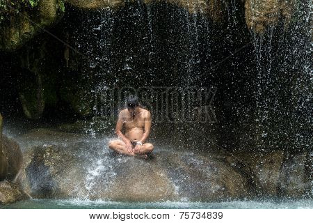 ERAWAN WATERFALL, THAILAND, JULY 08, 2013:  A Thai man is sitting under the Erawan waterfall. Many Thai people come here on the weekend to relax in the natural pools.  