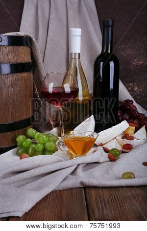Supper consisting of Camembert and Brie cheese, honey, wine and grapes on napkin and wine barrel on curtain background