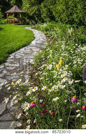 Wildflower garden with paved path leading to gazebo and blooming daisies