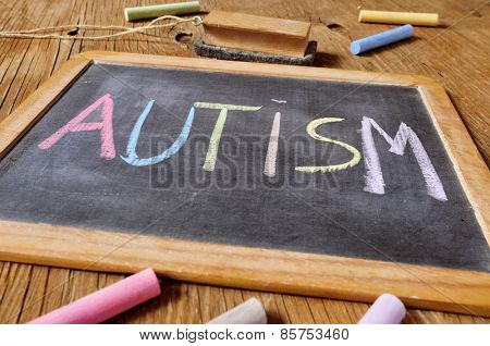 the word autism written with chalk of different colors in a chalkboard placed on a rustic wooden desk or table
