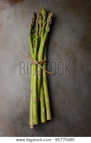 A single bunch of Asparagus tied with twine on a metal cooking sheet. Vertical format shot from a high angle. 