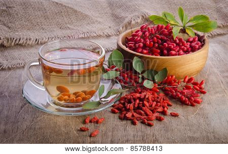 Goji Fresh Antioxidant Tea In Glass Cup And Barberries In Wooden Bowl