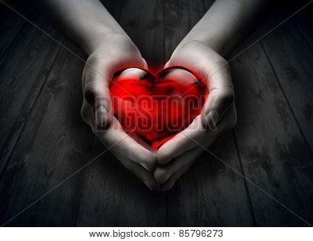 glass heart in the heart hand - wood background
