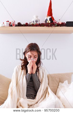 Portrait of a sick woman blowing her nose while sitting on the sofa