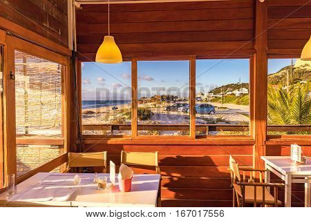 A beautifull sceen of the beach seen from the interior of a wooden cabin bar.