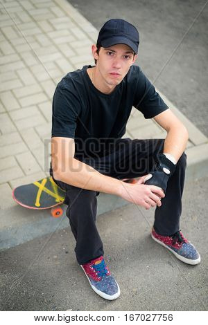Teenage skateboarder sitting on skateboard looking at camera