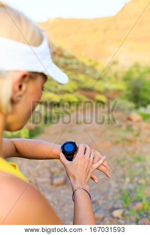Woman runner checking the elevation on sports watch smartwatch with altimeter app in summer mountains. Young girl training and running on mountain trail in the morning.