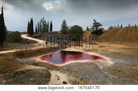 Unrecognized man walking near a Lake with red polluted toxic water of an Abandoned copper mine at Mitsero area in Cyprus