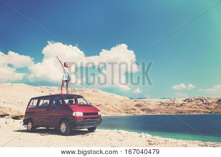 Beautiful tanned girl in a blue dress standing on a rooftop of red van and spreading arms. Post processed with vintage filter.