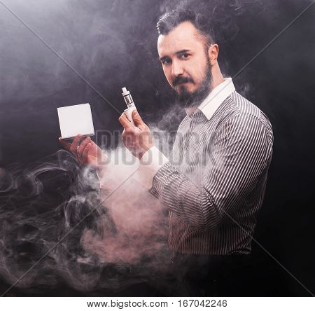 Vaping Man Holding A Mod And Box Of Vaponizer. A Cloud Of Vapor. Black Background.