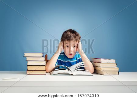 seven years old child reading a book at home. Boy studing at table on blue background