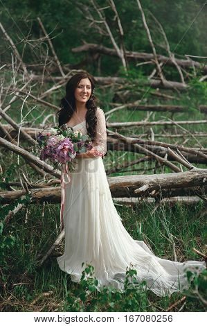 Beautiful bride in the forest with a large bouquet of different flowers. Boho style