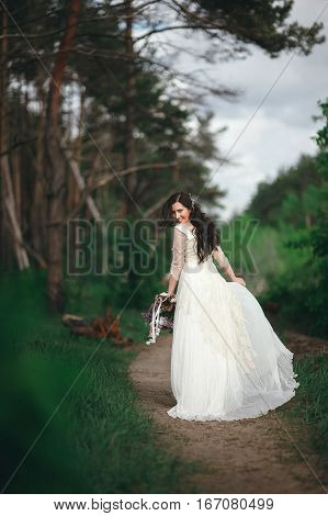 Beautiful bride in the forest with a large bouquet of different flowers. Boho style