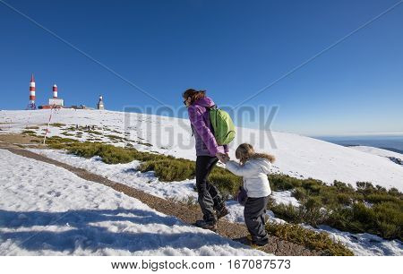 happy family winter scene of mother holding hands of three years old child hiking together in snow mountain summit of Navacerrada in Madrid Spain