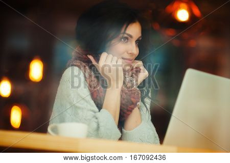 dreamer woman sittingin cafe at laptop with window