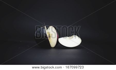 sliced black apple on a black background with a slice
