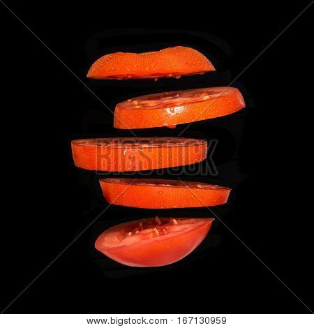 Flying tomato. Sliced red tomato isolated on black background. Levity vegetable floating in the air.